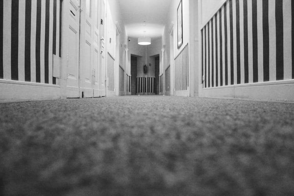 Close-up view of a beige carpet in a residential room, showing a textured surface with neatly aligned fibers. The carpet appears to be clean and well-maintained, with soft lighting highlighting its pl